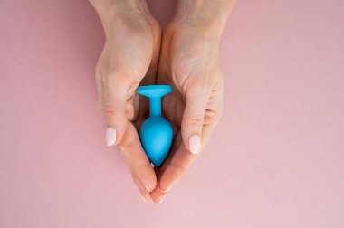 Bir kadın pembe arka planda mavi anal bir tıpa tutuyor. Alternatif seks için yetişkin oyuncağı
