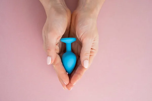 Een vrouw houdt een blauwe anale plug vast op een roze achtergrond. Volwassen speelgoed voor alternatieve seks — Stockfoto