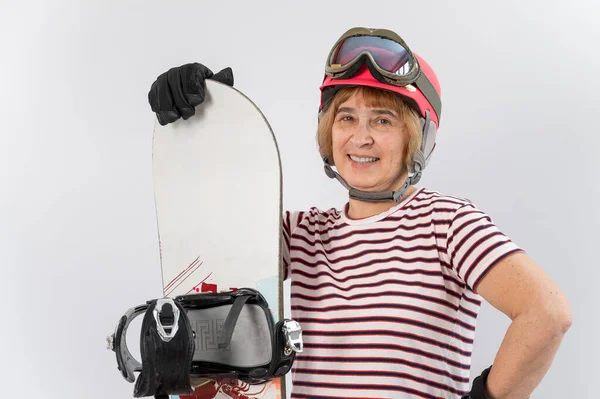 Porträtt av leende äldre kvinna i rosa skidhjälm handskar och med snowboard på vit bakgrund. — Stockfoto