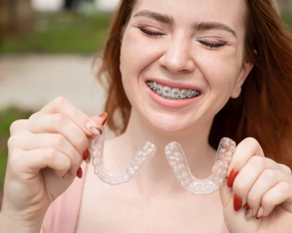 Krásná mladá rusovlasá žena s rovnátky na zubech drží odnímatelné podpěry venku — Stock fotografie
