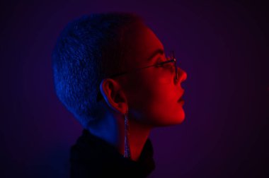 Kısa saçlı, neon ışıkta gözlük takan güzel bir genç kadının portresi.