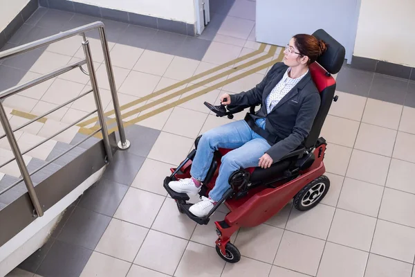 Caucasian woman in electric caterpillar wheelchair climbs up stairs. — Stock Photo, Image