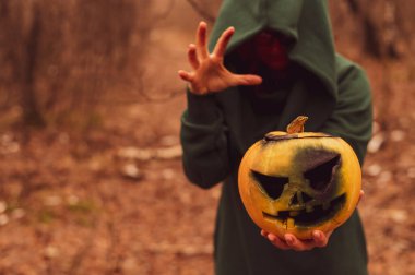 Ürkütücü bir cadı ormanın derinliklerinde balkabağı tutuyor. Fener Jack Cadılar Bayramı için sarı duman yayar