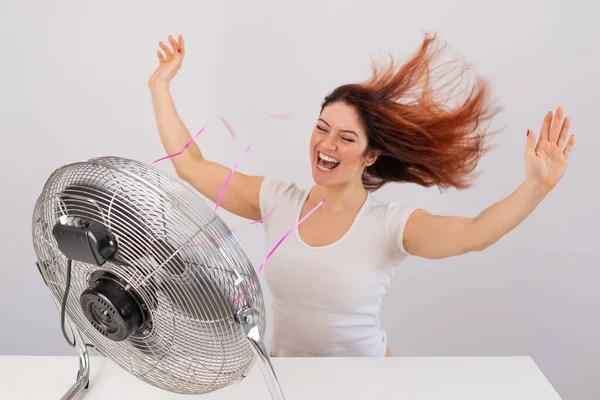 Alegre mujer caucásica disfrutando del viento soplando de un ventilador eléctrico sobre un fondo blanco. — Foto de Stock