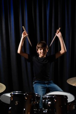 Çocuk stüdyoda davul çalmayı siyah bir arkaplanda öğreniyor. Müzik okulu öğrencisi
