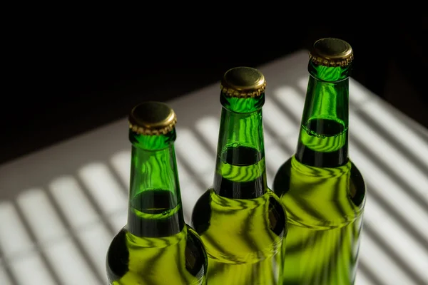 Tři skleněné láhve od piva ve stínu žaluzií. — Stock fotografie
