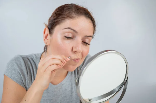 Λευκή γυναίκα κοιτιέται στον καθρέφτη και αφαιρεί η ίδια το μουστάκι με τη βοήθεια τσιμπιδάκι. Υπερτρίχωση. — Φωτογραφία Αρχείου