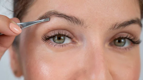 Retrato de cerca de una mujer caucásica que se corrige las cejas con pinzas — Foto de Stock