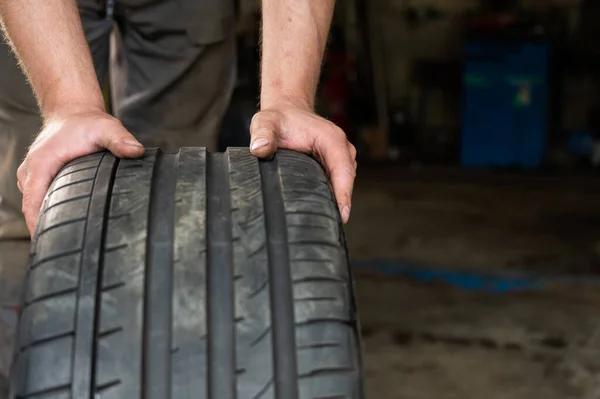 An auto mechanic holds a wheel of a car. Change of car tires according to the season — Stock Photo, Image