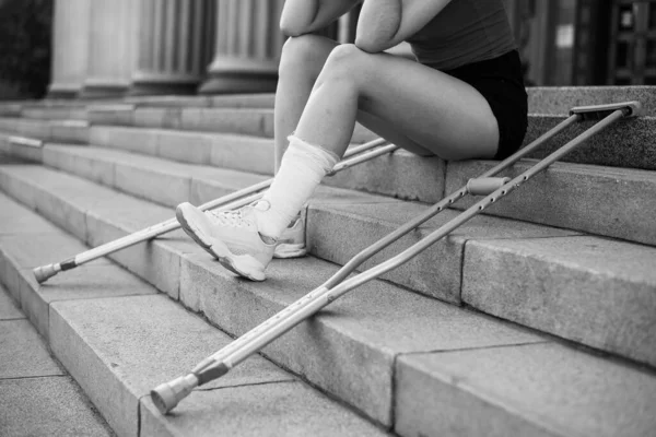 Fille avec blessure à la jambe est assis sur les escaliers avec des béquilles. — Photo