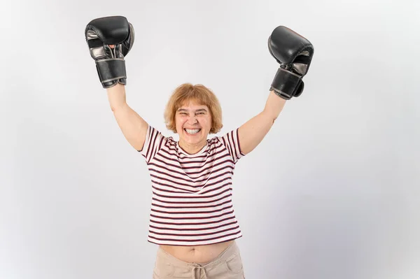 一位戴着格斗手套的老年妇女在白色背景下举起双手。决斗中的胜利 — 图库照片