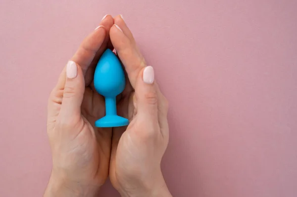 Seorang wanita memegang anal biru plug pada latar belakang merah muda. Mainan dewasa untuk seks alternatif — Stok Foto