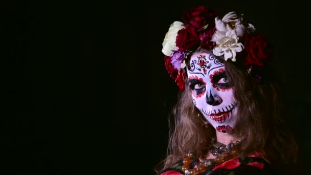 Kvinna i Santa Muerte makeup på en svart bakgrund. Flicka klädd i traditionell mexikansk helig dödsdräkt för halloween. — Stockvideo