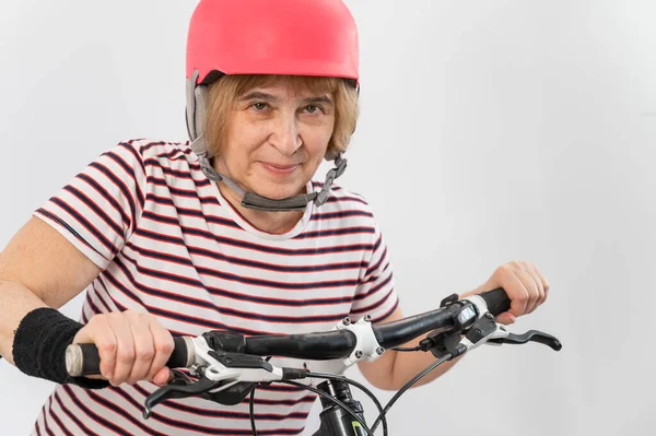 Mujer mayor con casco rosa en bicicleta sobre fondo blanco. — Foto de Stock
