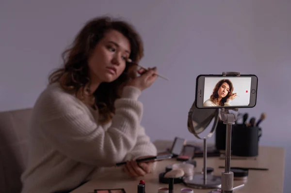 Junge Kaukasierin nimmt ein Online-Schminktraining-Video auf ihrem Handy auf. Video-Bloggerin schminkt sich. — Stockfoto