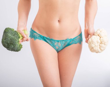 İç çamaşırlı yüzü olmayan bir kadın beyaz arka planda karnabahar ve brokoli tutuyor. Yiyecek alışkanlıkları.