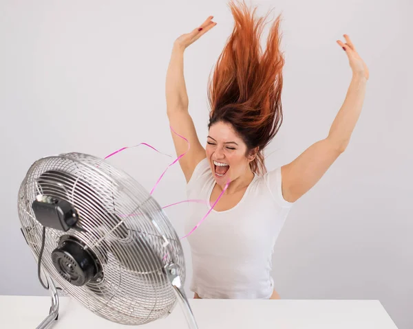 Joyeuse femme caucasienne profitant du vent soufflant d'un ventilateur électrique sur un fond blanc. — Photo