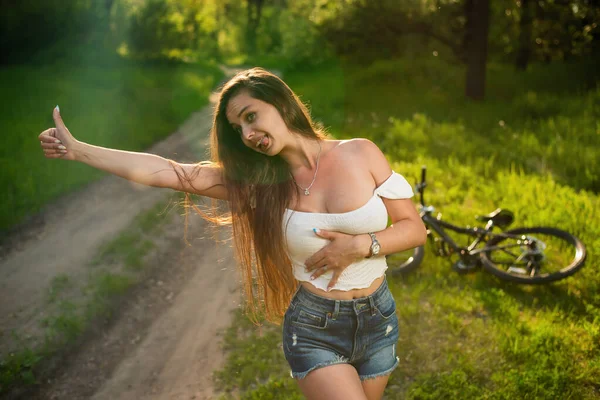 Joven mujer sexy con bicicleta rota y en busca de ayuda para levantar el pulgar —  Fotos de Stock