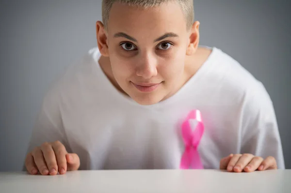 Mulher com um corte de cabelo loiro curto com uma fita rosa em uma camiseta branca como um símbolo de câncer de mama em um fundo branco. — Fotografia de Stock