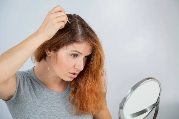 Mujer caucásica encuentra el pelo gris y lo quita con pinzas. Signos de envejecimiento. — Foto de Stock