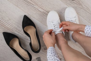 İş kadını beyaz deri ayakkabıları çıkarıp siyah yüksek topuklu ayakkabılar giyer. Kız işten önce ayakkabılarını değiştiriyor.
