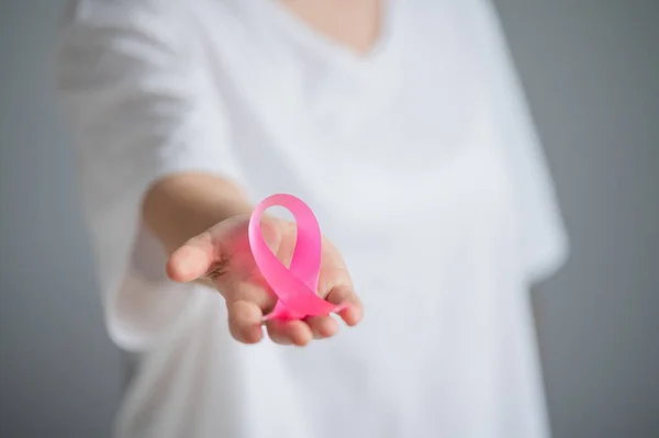 Uma mulher sem rosto usando uma camiseta branca segura uma fita rosa como um símbolo de câncer de mama em um fundo branco. — Fotografia de Stock