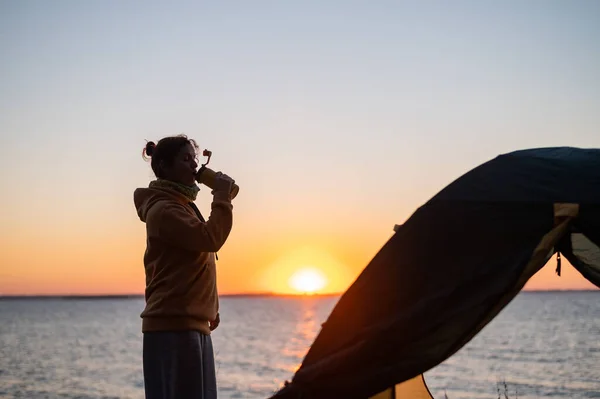 Kvinnan vilar i ett tält i naturen vid solnedgången. Flickan satte upp läger på flodstranden — Stockfoto