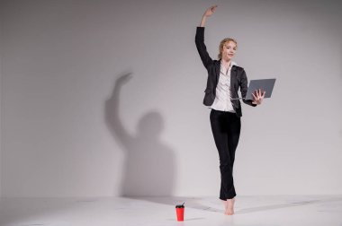 İş elbisesi giymiş çıplak ayaklı balerin dizüstü bilgisayara poz veriyor ve kahve içiyor. Bilgisayar başında esnek bir kadın çalışıyor.