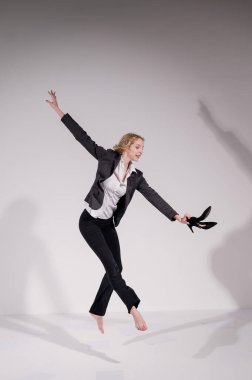 Beyaz bir arka planda ayakkabıları ile atlayan takım elbiseli zarif çıplak ayaklı bir balerin..