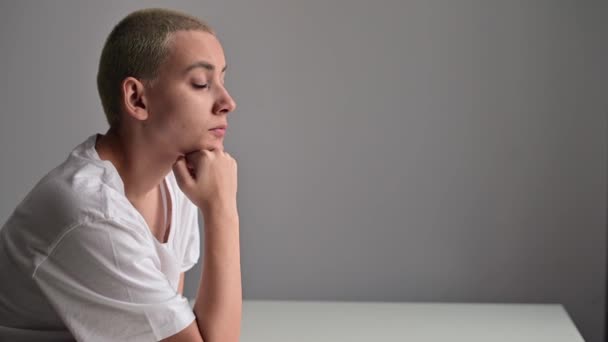 Porträtt av en ledsen ung kvinna sitter vid ett bord på en vit bakgrund. Kopiera utrymme — Stockvideo