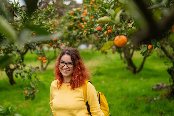 Rudovlasá usmívající se žena stojí v mandarinkové zahradě. — Stock fotografie