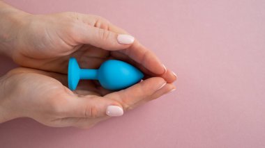 Bir kadın pembe arka planda mavi anal bir tıpa tutuyor. Alternatif seks için yetişkin oyuncağı