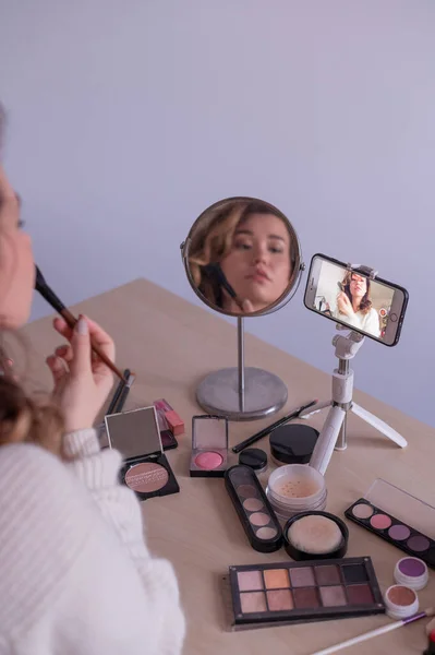 Mulher caucasiana leva uma lição de maquiagem on-line para si mesma em seu telefone celular — Fotografia de Stock