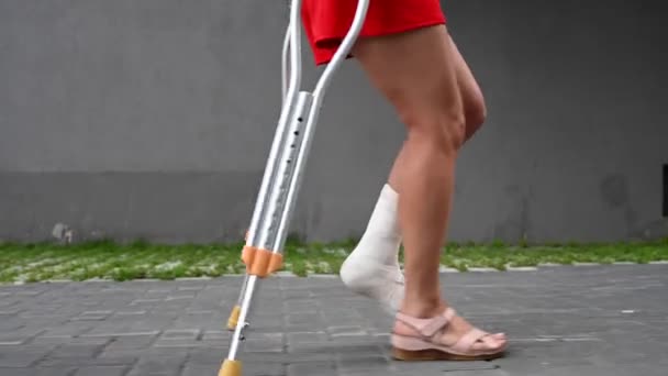 Ayağı kırık bir kadın koltuk değnekleriyle sokakta yürüyor.. — Stok video