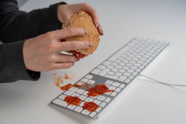 Žena bez tváře jí burger a kape jí kečup na klávesnici. — Stock fotografie