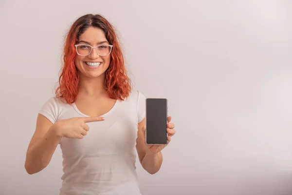 Kafkasyalı bir kadın beyaz arka planda boş ekranlı bir akıllı telefonu işaret ediyor. — Stok fotoğraf