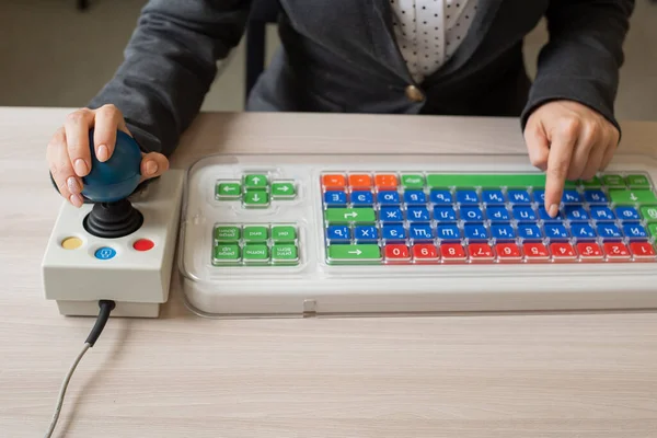 An unrecognizable woman with cerebral palsy is typing on the keyboard. A girl with disabilities works on a specially equipped computer — Stock Photo, Image