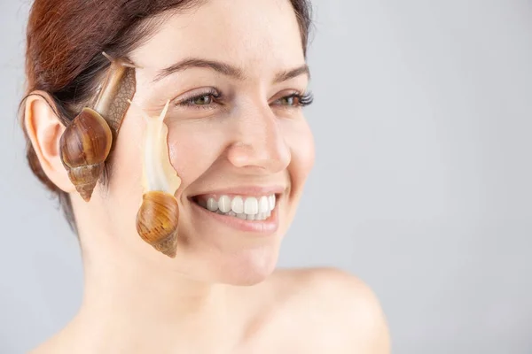 Hermosa mujer caucásica sonriente con caracoles en la cara. Terapia de rejuvenecimiento de la piel. — Foto de Stock