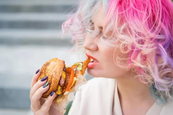 Кавказька жінка з кучерявим волоссям їсть бургер. Погані звички в харчуванні і любов до фаст - фуду. — стокове фото