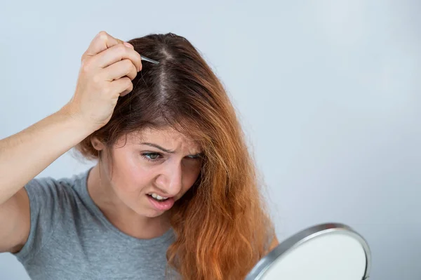 Mujer caucásica encuentra el pelo gris y lo quita con pinzas. Signos de envejecimiento. — Foto de Stock