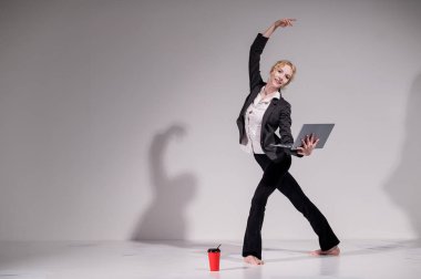 İş elbisesi giymiş çıplak ayaklı balerin dizüstü bilgisayara poz veriyor ve kahve içiyor. Bilgisayar başında esnek bir kadın çalışıyor.