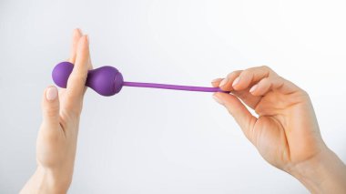 Beyaz arka planda pelvik zemin kaslarını çalıştırmak için elektronik Kegel antrenörü tutan yüzü olmayan bir kadın. Seks oyuncağı akıllı telefonla senkronize edildi
