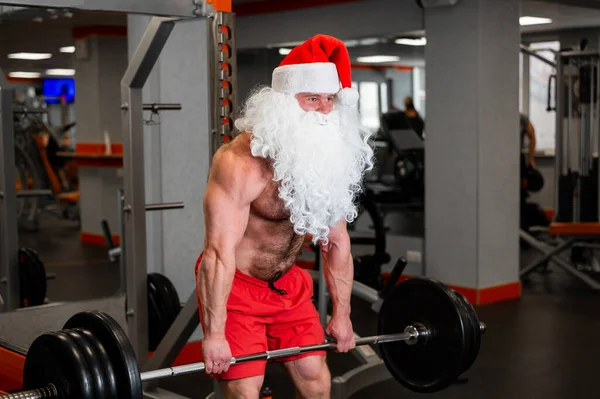 Święty Mikołaj na siłowni. Muskularny mężczyzna z nagim tułowiem ćwiczący z hantlami. — Zdjęcie stockowe