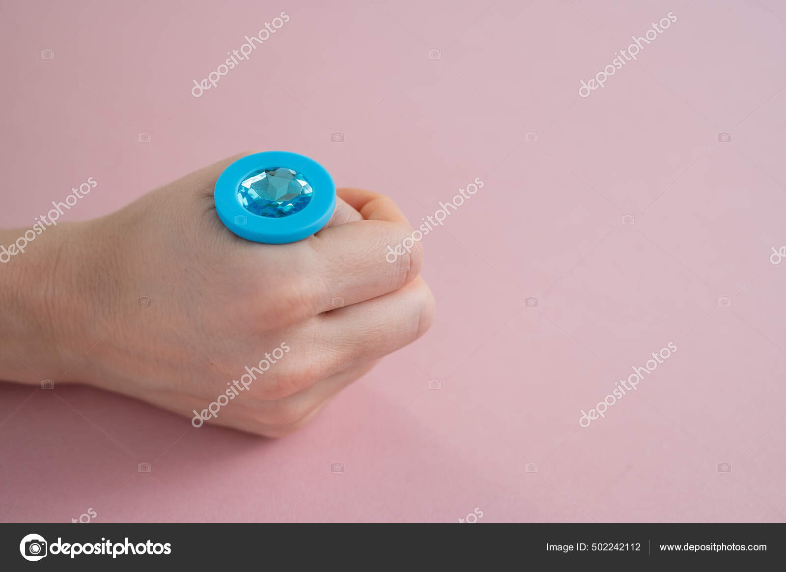A woman is holding a blue butt plug with a crystal on a pink background pic
