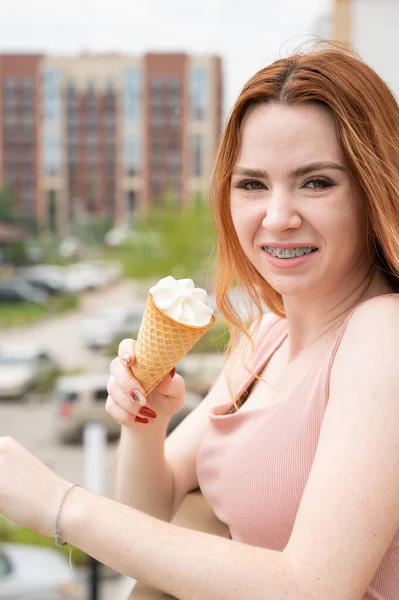 Retrato de una joven hermosa pelirroja sonriendo con frenillos y yendo a comer helado al aire libre en verano —  Fotos de Stock
