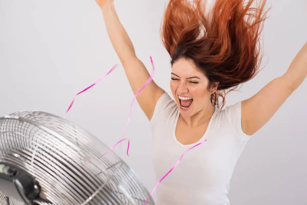 Радостная белая женщина наслаждается ветром, дующим от электрического вентилятора на белом фоне. — стоковое фото