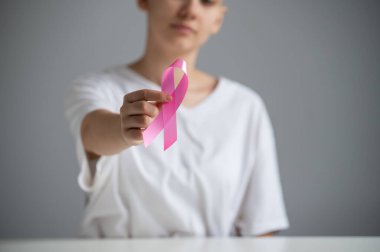 Beyaz tişört giyen yüzü olmayan bir kadın beyaz arka planda göğüs kanserinin sembolü olarak pembe bir kurdele tutuyor..