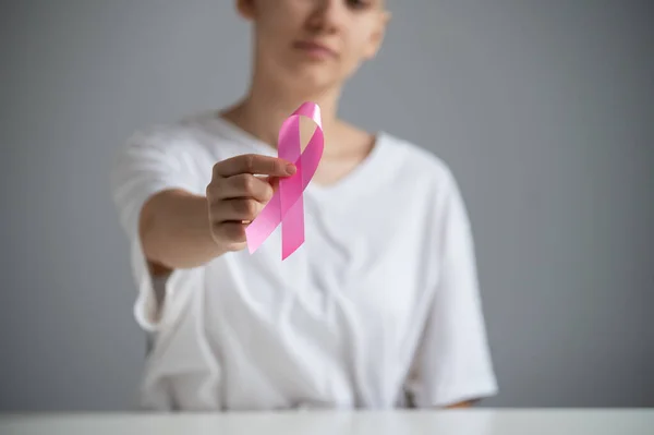 Uma mulher sem rosto usando uma camiseta branca segura uma fita rosa como um símbolo de câncer de mama em um fundo branco. — Fotografia de Stock