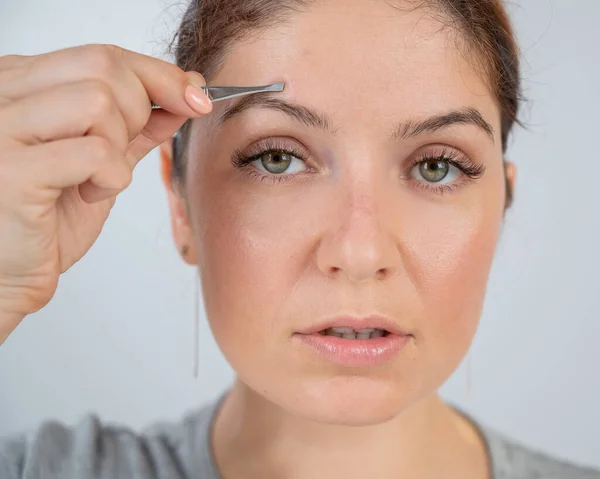 Retrato de close-up de uma mulher caucasiana fazendo correção de sobrancelha com pinças — Fotografia de Stock