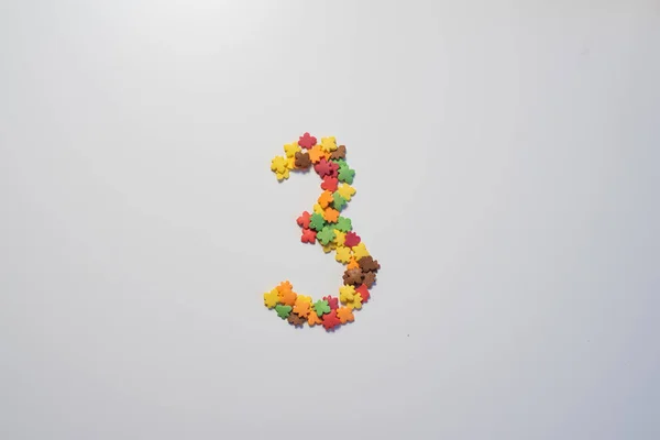 Numerale tre da pasticceria dolce guarnizione sotto forma di fogliame colorato su sfondo bianco. — Foto Stock